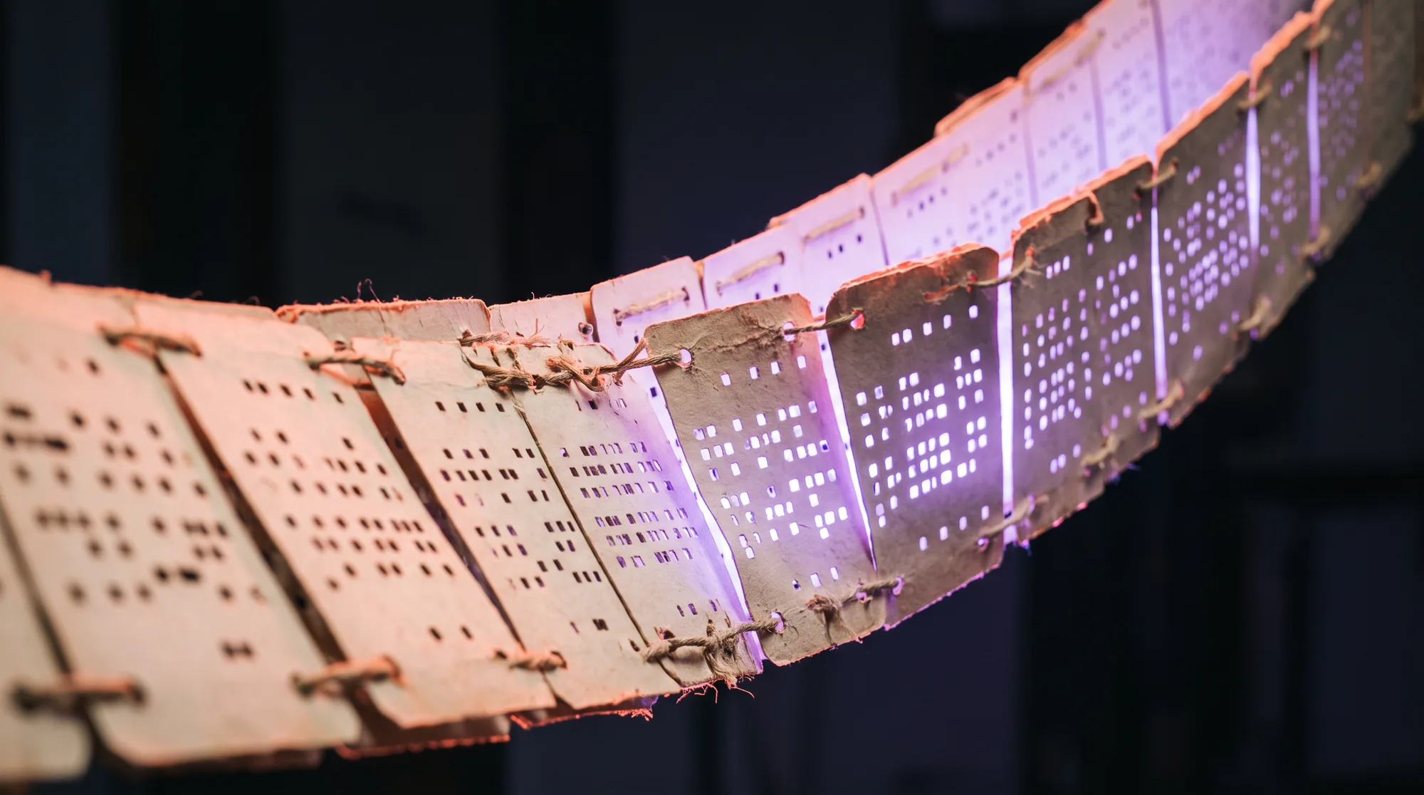 Punched cards linked in a chain, holes catching the light.